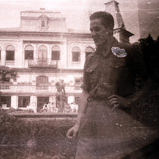 Military officer in front of colonial-era mansion.