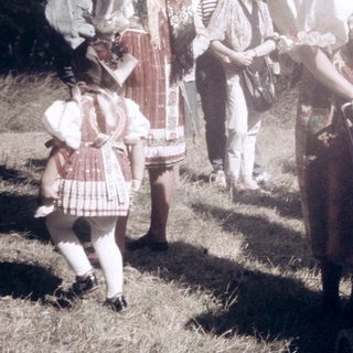 Group in traditional folk costumes milking cow outdoors.