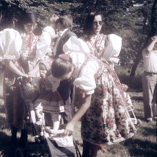 Group in traditional folk costumes milking cow outdoors.