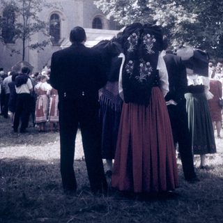 Traditional folk costumes in outdoor gathering near church.