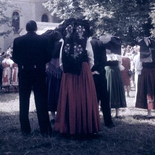 Traditional folk costumes in outdoor gathering near church.