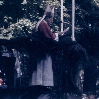 Outdoor gathering with speaker addressing seated audience.