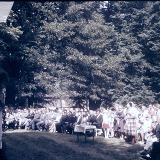Outdoor gathering with speaker addressing seated audience.