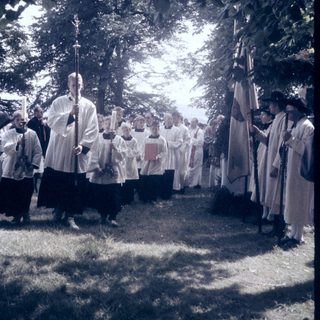 Group of clergy in white robes holding candles outdoors.