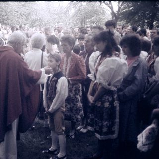 Outdoor religious blessing ceremony with priest and children.
