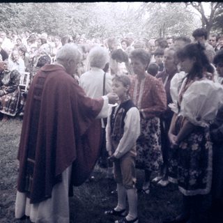 Outdoor religious blessing ceremony with priest and children.