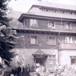 Historic wooden building with gathering of people outside.