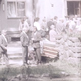 Historic wooden building with gathering of people outside.