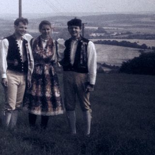 Three people in traditional attire posing on a hillside.