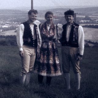 Three people in traditional attire posing on a hillside.