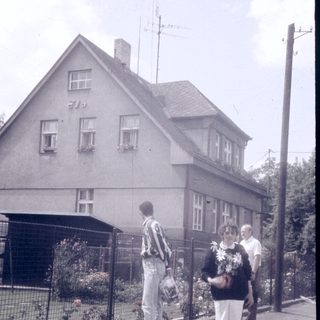 People walking near a two-story house with a gated garden.