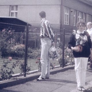 People walking near a two-story house with a gated garden.