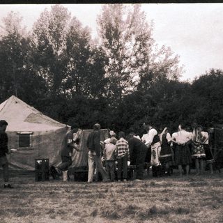 Group of people gathered outside canvas tents in outdoor setting.