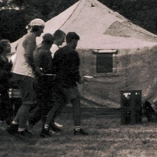 Group of people gathered outside canvas tents in outdoor setting.