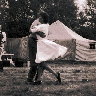 Couple dancing outdoors near tents.