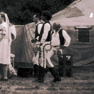 Group in traditional folk costumes dancing outdoors.