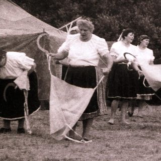 Group of women and girls playing outdoor game with rackets.