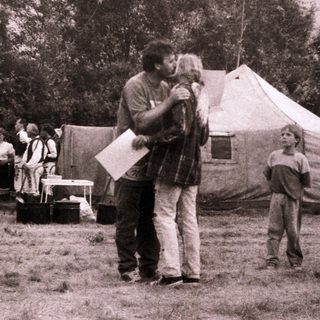 Man hugging child at outdoor gathering near tents.