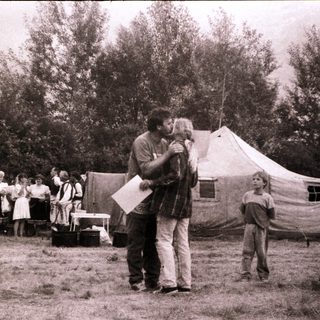 Man hugging child at outdoor gathering near tents.