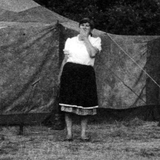 Camp setting with man demonstrating archery to onlookers.