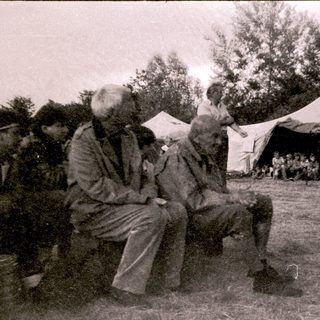 Two elderly men sitting outdoors near tents.