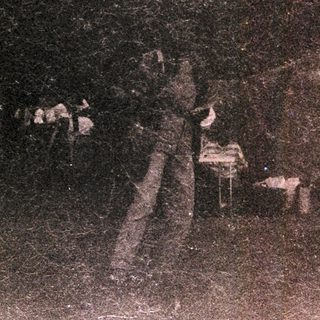Vintage photo of tented campsite in wooded area.