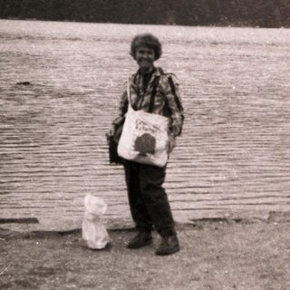 Child holding bags by a lake near mountains.