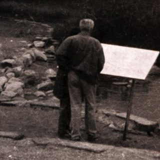 Artist painting lakeside with mountains in background.