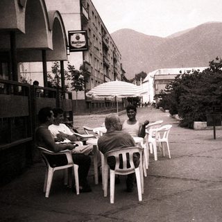 People sitting outdoors near mountains in urban café setting.