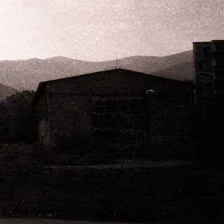 Industrial smokestack and factory ruins in hilly landscape.