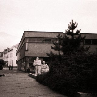 Urban street scene with Soviet-era statues and buildings.