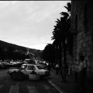 Busy coastal town street with parked cars and pedestrians.