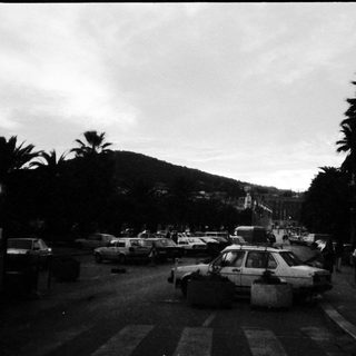 Busy coastal town street with parked cars and pedestrians.
