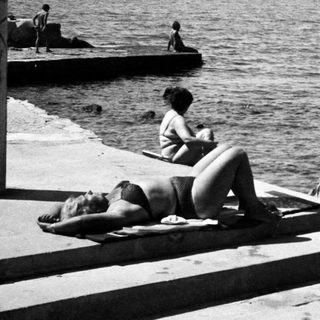 Sunbathing by seaside pier, mid-20th century.