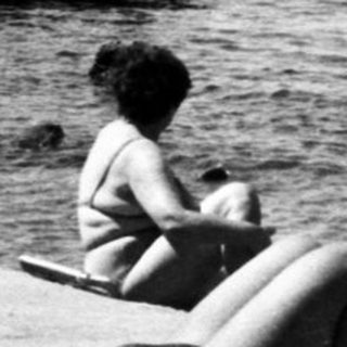 Sunbathing by seaside pier, mid-20th century.