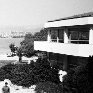 Coastal building with man sitting on steps overlooking water.