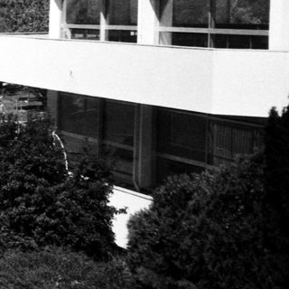 Coastal building with man sitting on steps overlooking water.