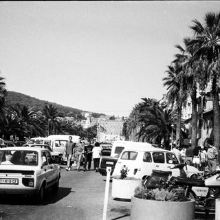 Busy coastal street with parked cars, pedestrians, and palm trees.