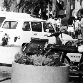 Busy coastal street with parked cars, pedestrians, and palm trees.