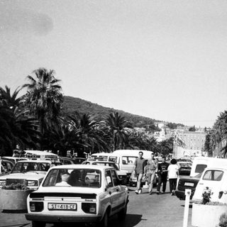Busy coastal street with parked cars, pedestrians, and palm trees.