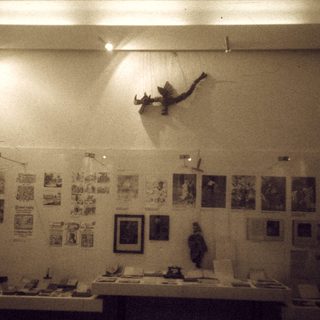 Art exhibition with framed prints, sculptures, and a suspended bird figure.