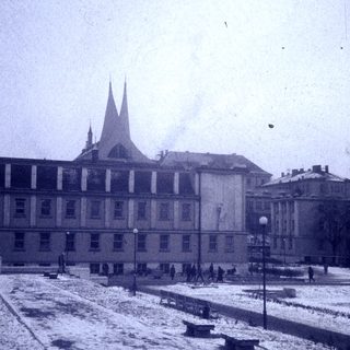 Historic building in snowy plaza with spired roof.