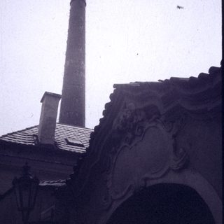 Industrial chimney beside ornate classical building rooftop.