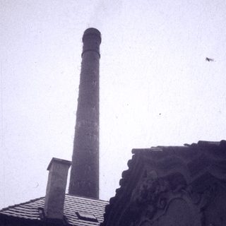 Industrial chimney beside ornate classical building rooftop.