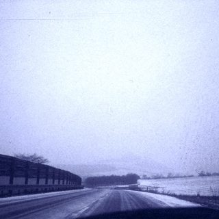 Snow-covered rural road with train tracks.