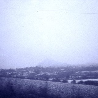 Snow-covered rural landscape with distant hill.