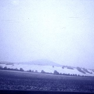 Snow-covered landscape with distant hills and trees.