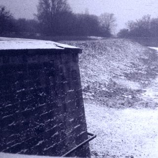 Snow-covered rural road with tracks, industrial buildings.