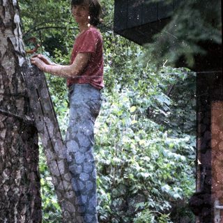 Woman climbing wet tree ladder in rainforest.