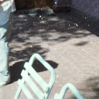 Two elderly people sitting and standing outdoors on a rainy day.